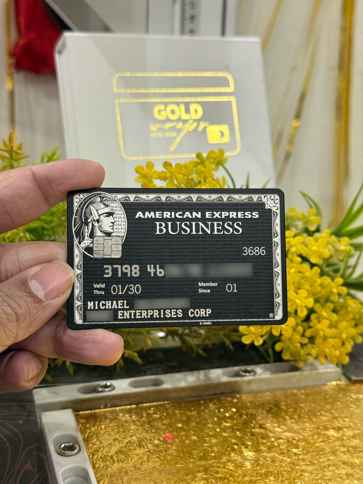 American Express Business card held by a hand with yellow flowers in the background